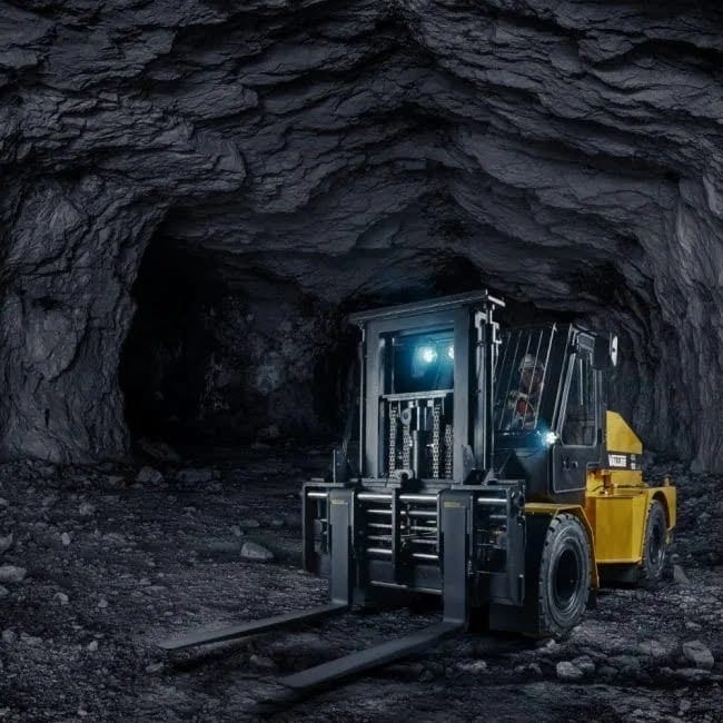 Forklift inside a dark mining tunnel, operator visible in the cab with headlights illuminating rocky walls and forks lowered.